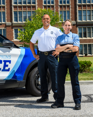 Two Police officers stand next to patrol car.